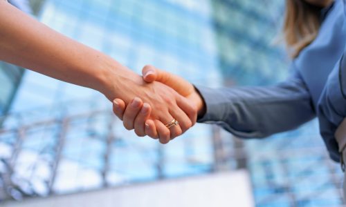 Woman handshaking outdoors over modern glass business building background, close-up picture